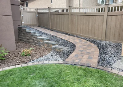 a backyard with a stone walking path by Lush Landscaping