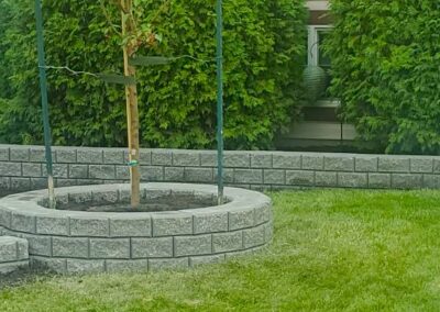 a backyard with two tree planters with stone retaining walls around them built by Lush Landscaping