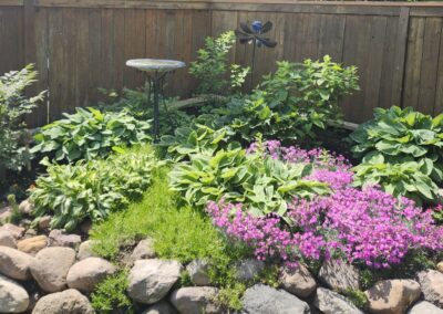 Flowers, plants, stones and bushes planted in a backyard garden by Lush Landscaping