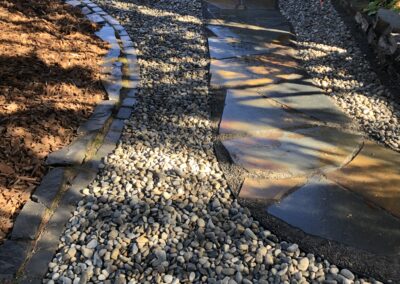 Stone walkway with drainage rocks beside it by Lush Landscaping