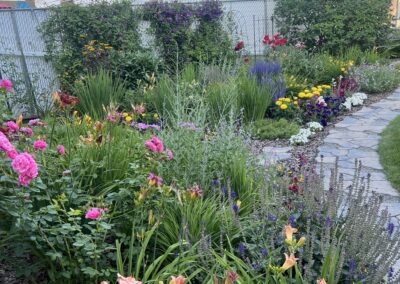 A backyard with a stone walkway and many beautiful colorful flowers that were planted by Lush Landscaping