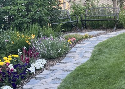 A backyard with a stone walkway and many beautiful colorful flowers that were planted by Lush Landscaping