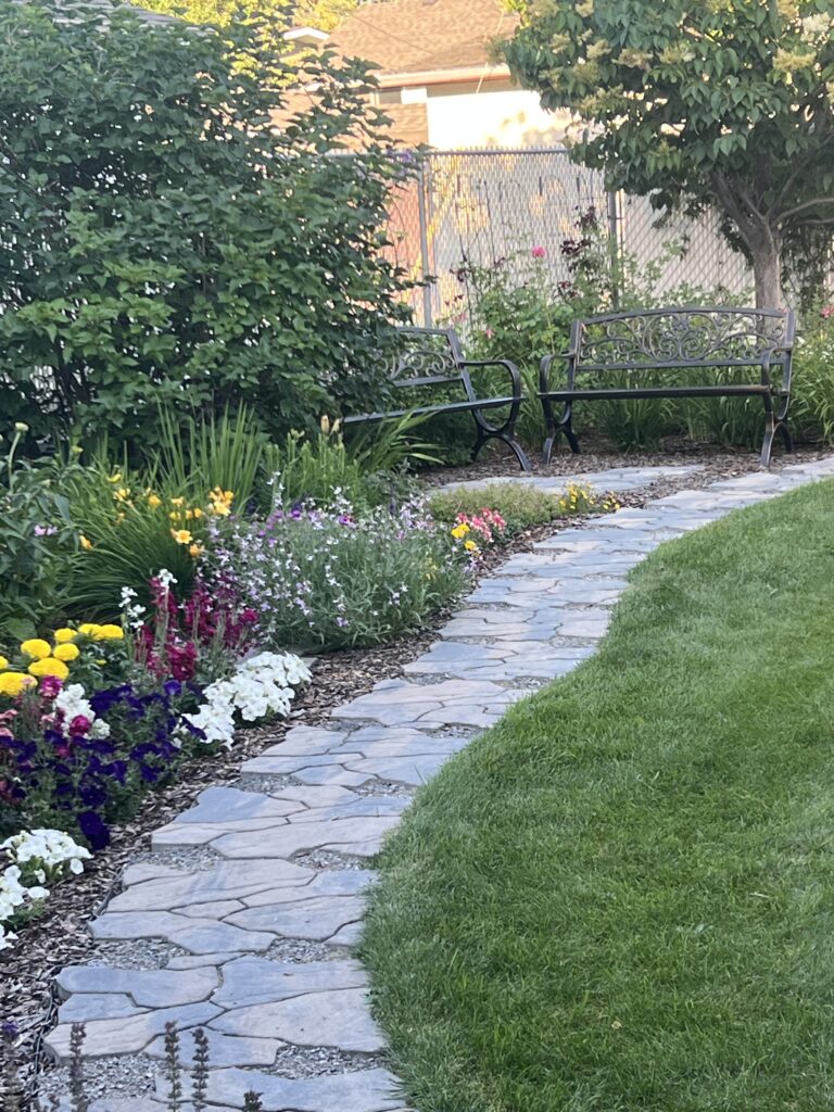 A backyard with a stone walkway and many beautiful colorful flowers that were planted by Lush Landscaping