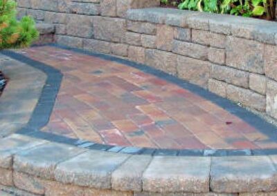 A close-up view of stone steps with following footpath and deck area incorporated into a low retaining wall part of a garden landscape design.