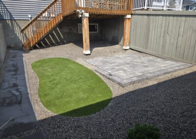 a backyard filled with gravel with a patio and a small patch of grass