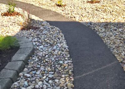 a backyard with a paved walkway and decorative rocks on either side that was completed by Lush Landscaping in Edmonton